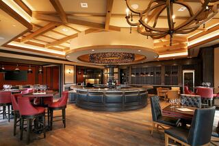 An upscale restaurant features a circular bar, intimate seating areas, and elegant decor with wooden accents and soft lighting.