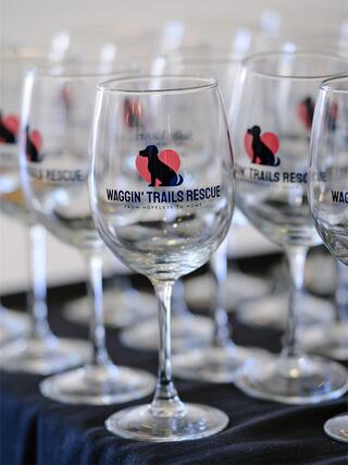 A collection of wine glasses featuring the "Waggin' Trails Rescue" logo, promoting a message of hope and animal rescue.