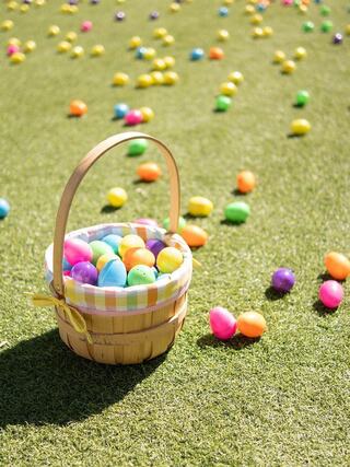 A woven basket filled with colorful plastic eggs sits on bright green grass, surrounded by scattered eggs in various vibrant colors.