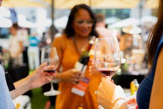 A vibrant outdoor event showcases wine tasting, with attendees enjoying glasses of red wine and mingling in a festive atmosphere.