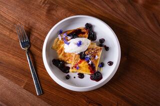 Delicate crepes topped with whipped cream, berry sauce, and edible flowers, served on a white plate, exuding elegance and flavor.