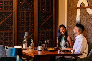 A couple enjoys a cozy dinner, sharing smiles and wine, surrounded by an elegant wine cellar and a warm atmosphere.