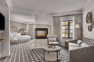 A stylish hotel suite featuring a cozy fireplace, modern furnishings, a comfortable seating area, and large windows with natural light.