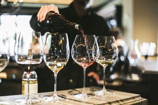 A person pours red wine into a glass among several empty glasses, creating an elegant atmosphere in a lively setting.