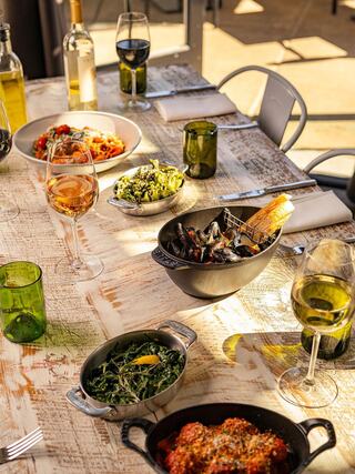 A beautifully arranged dining table features an array of gourmet dishes, including pasta, seafood, and vibrant salads, accompanied by wine.