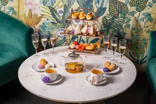 A stylish tea setup features an array of delicate pastries, sparkling drinks, and vibrant floral decor on a marble table.