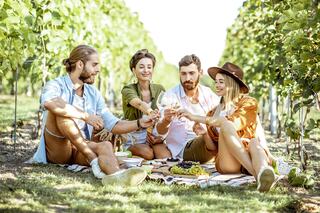 Four friends enjoy a sunny picnic in a vineyard, sharing wine and laughter among grapevines, creating a joyful and relaxed atmosphere.