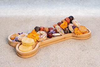 A wooden bone-shaped platter filled with colorful treats, flowers, and cookies, perfect for a pet-themed celebration or gathering.