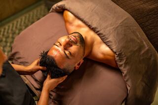 A man relaxes on a treatment table while receiving a soothing head massage, creating a serene and tranquil atmosphere.