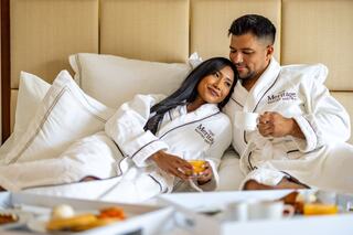 A couple in cozy robes relaxes on a bed, enjoying breakfast together, radiating warmth and intimacy.