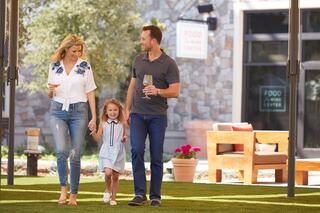A happy family strolls together outdoors, enjoying drinks and bright sunshine, with a casual and joyful atmosphere.